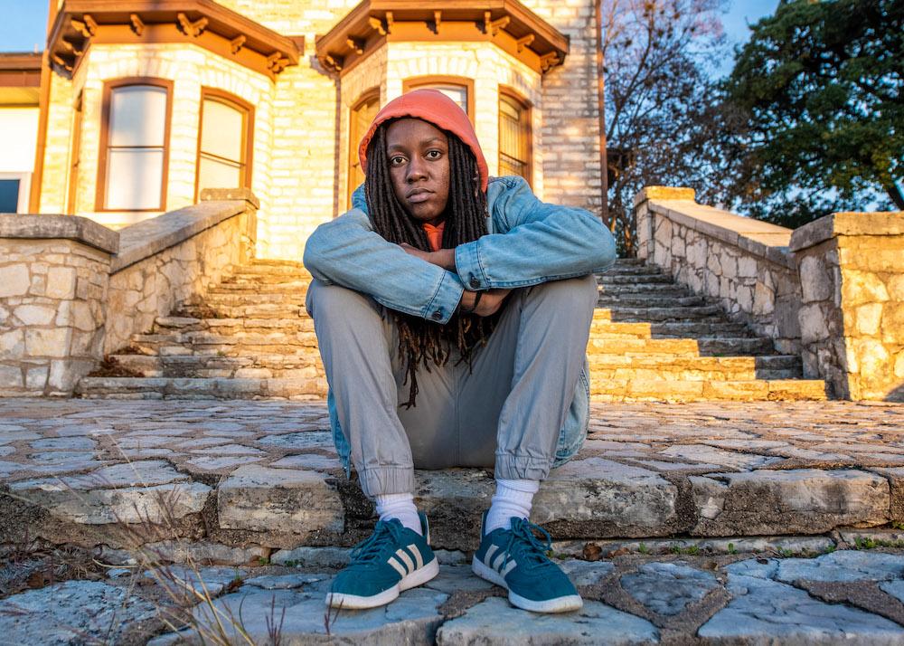 Blakchyl seated on stone steps outside an East Austin home