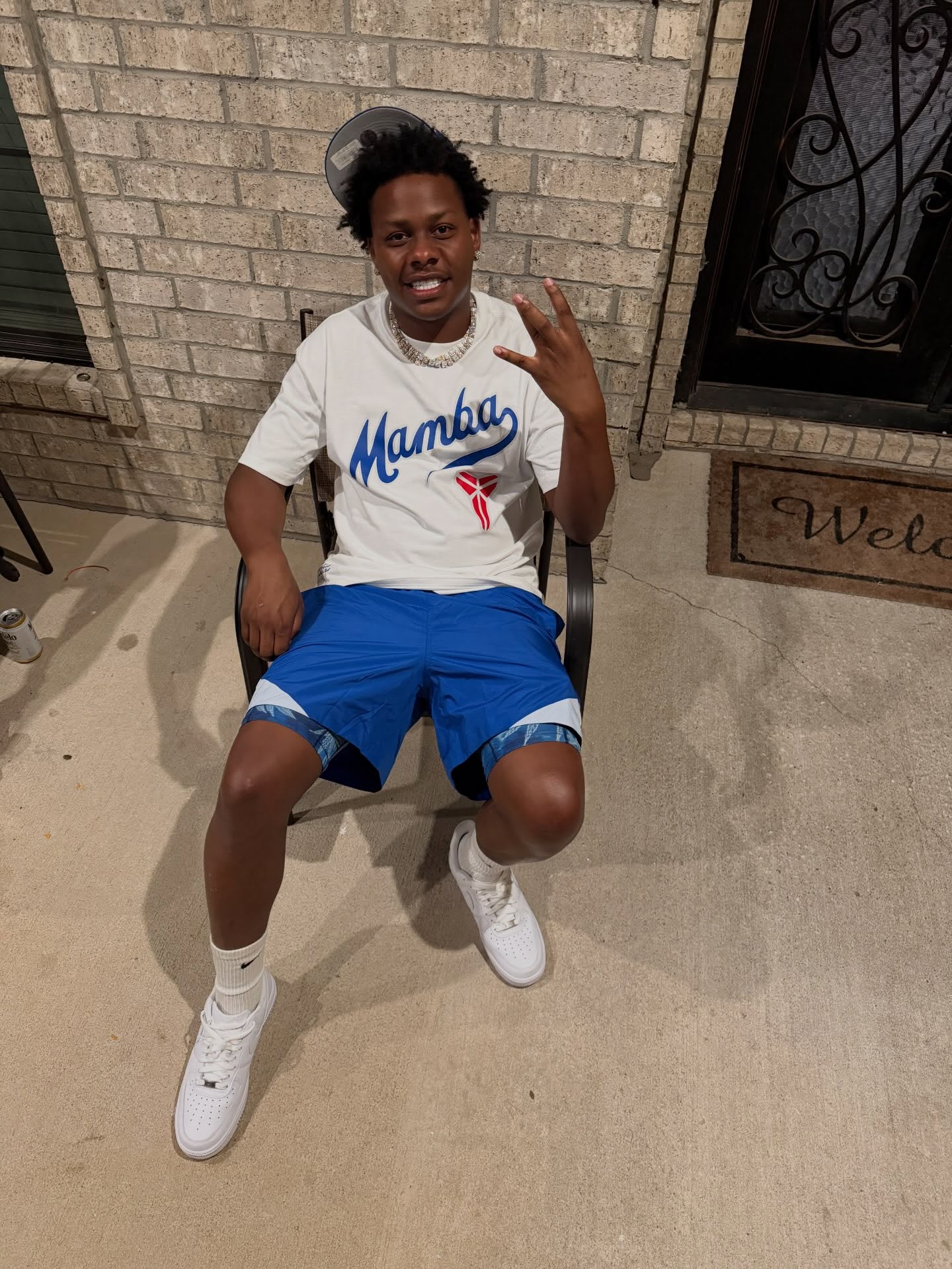 Cootie seated outside wearing a white Mamba shirt and blue shorts