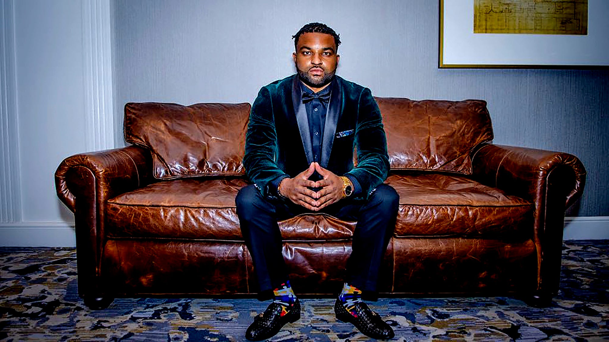 J French seated on a leather couch in a dark green velvet jacket
