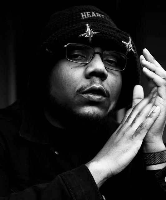 J Soulja wearing glasses and a knit cap in a black-and-white portrait