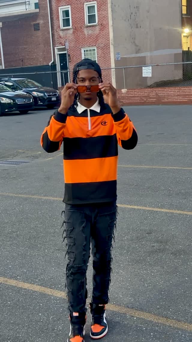 Kane Kuhtti standing outdoors in orange and black while adjusting sunglasses