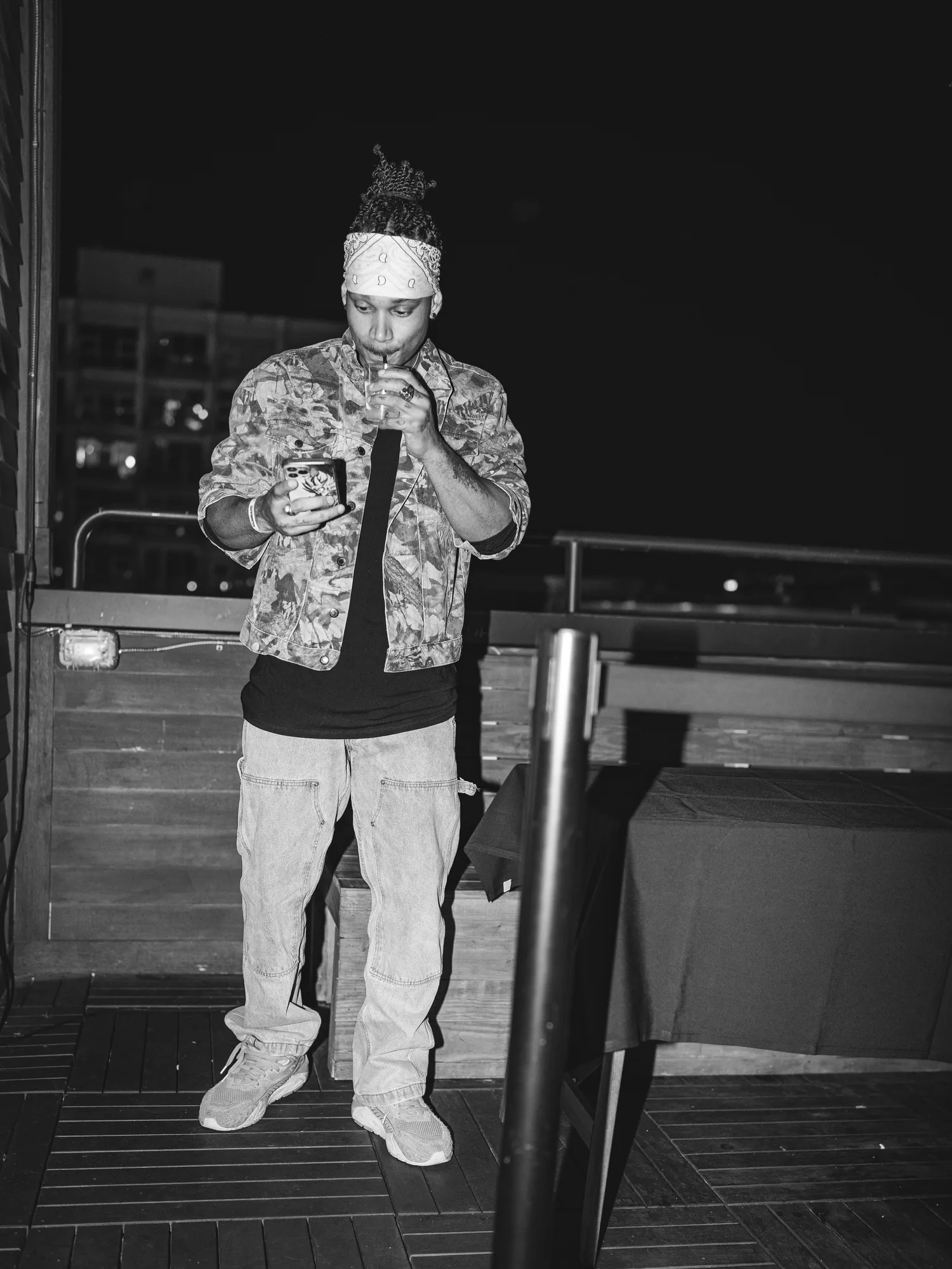 RIIIVER JORDAN sipping a drink on an outdoor patio at night