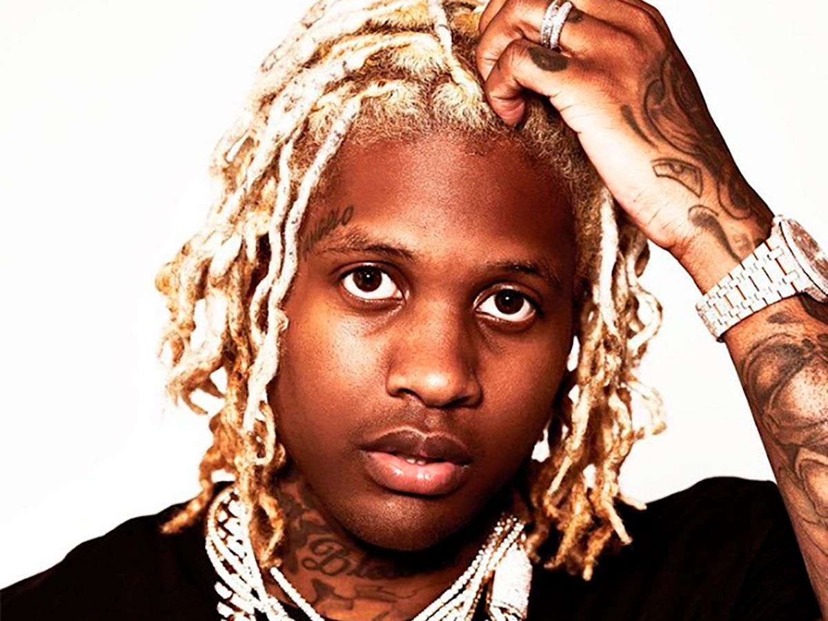 Lil Durk in a black shirt and layered chains against a white background